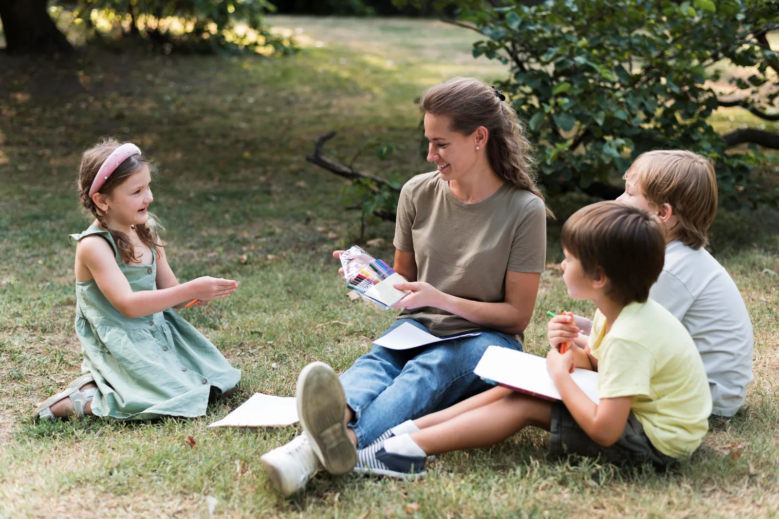 A teacher and children sitting on the grass outdoors during a summer English program